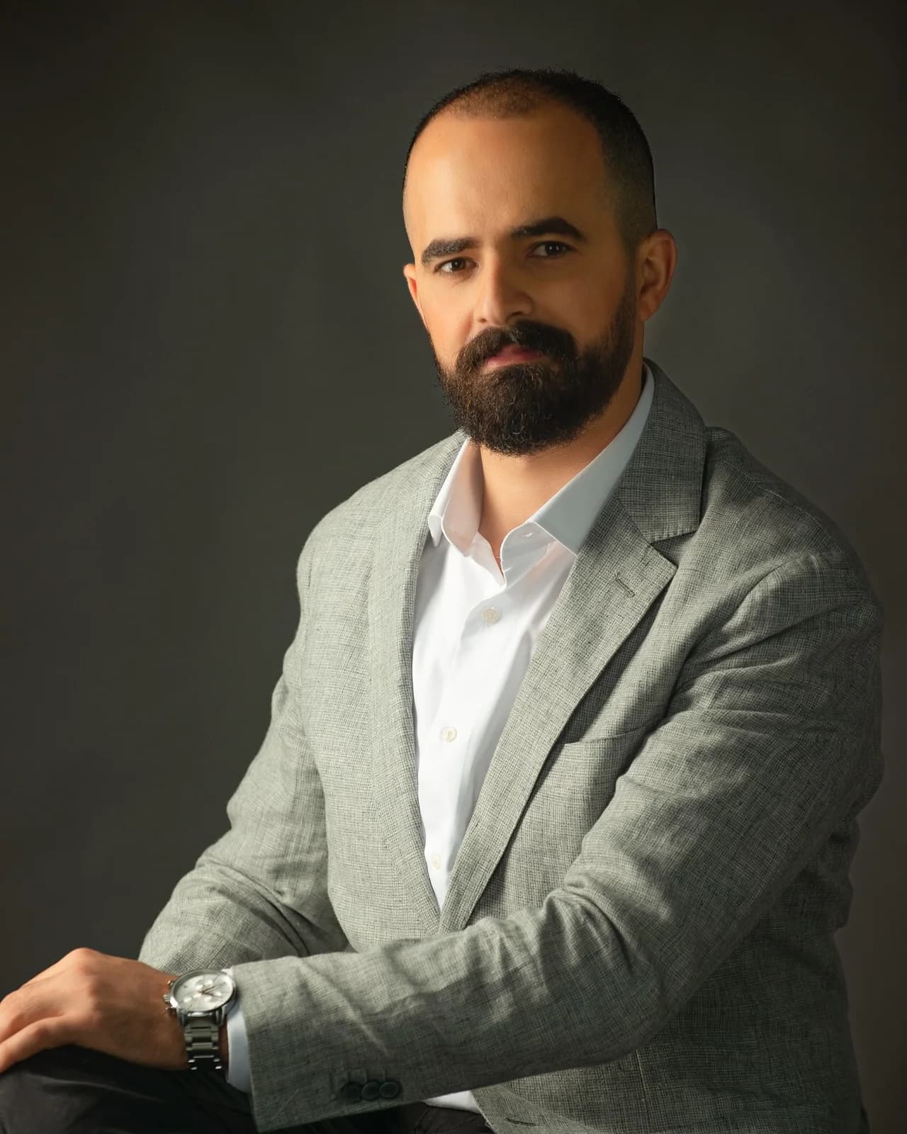 Arch. Waleed Alsharif, founder and director of Petra Point, seated in a grey linen jacket against a dark studio background.